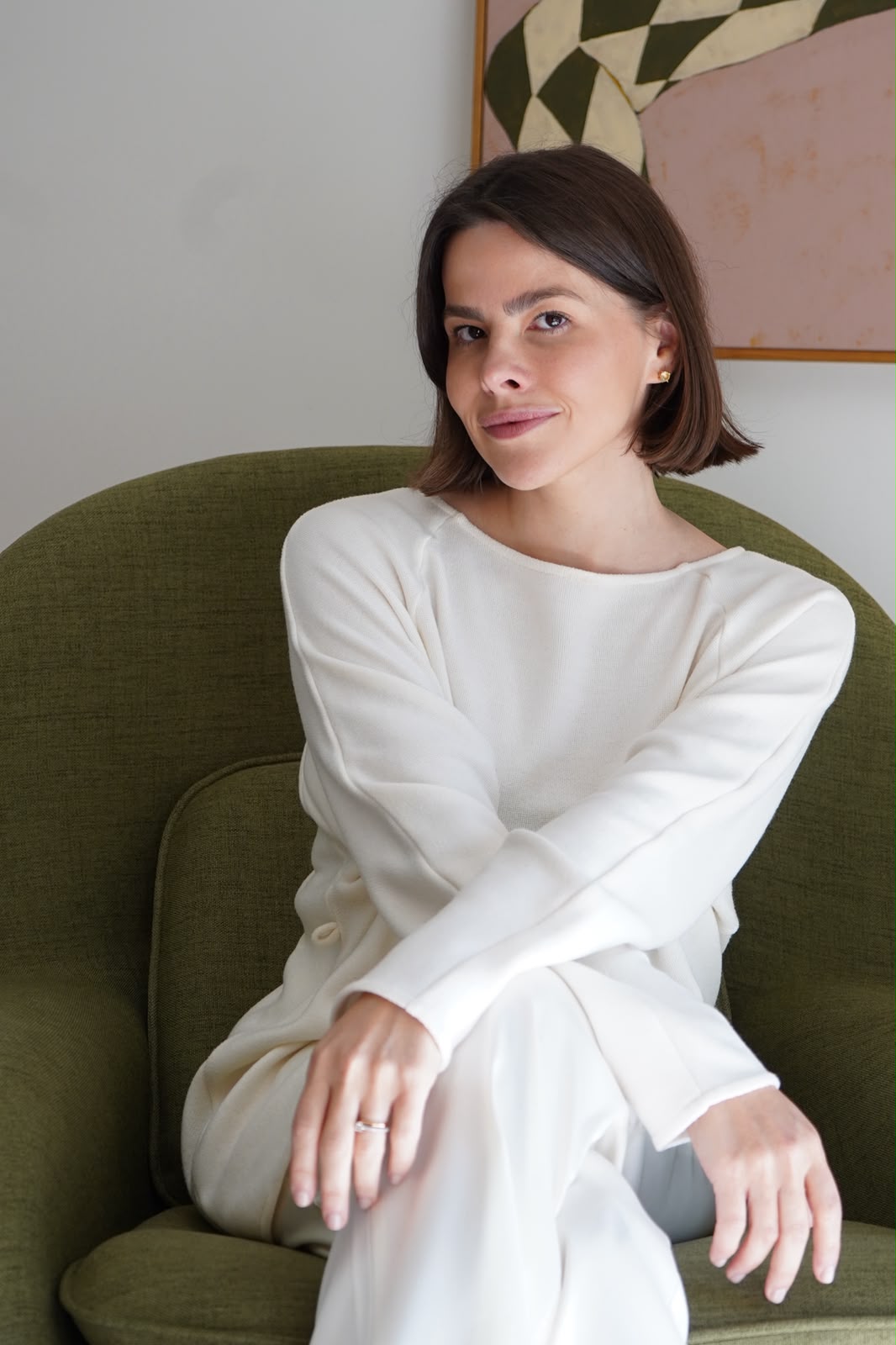 Drª. Gabriela Noronha sentada em poltrona verde da clínica, vestindo tricô off-white